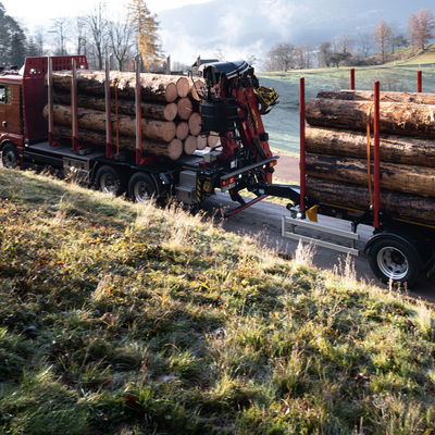 LKW mit Zentralachsanhänger von DOLL fährt im Morgengrauen über eine schmale Landstraße zwischen Wiesen und Feldern